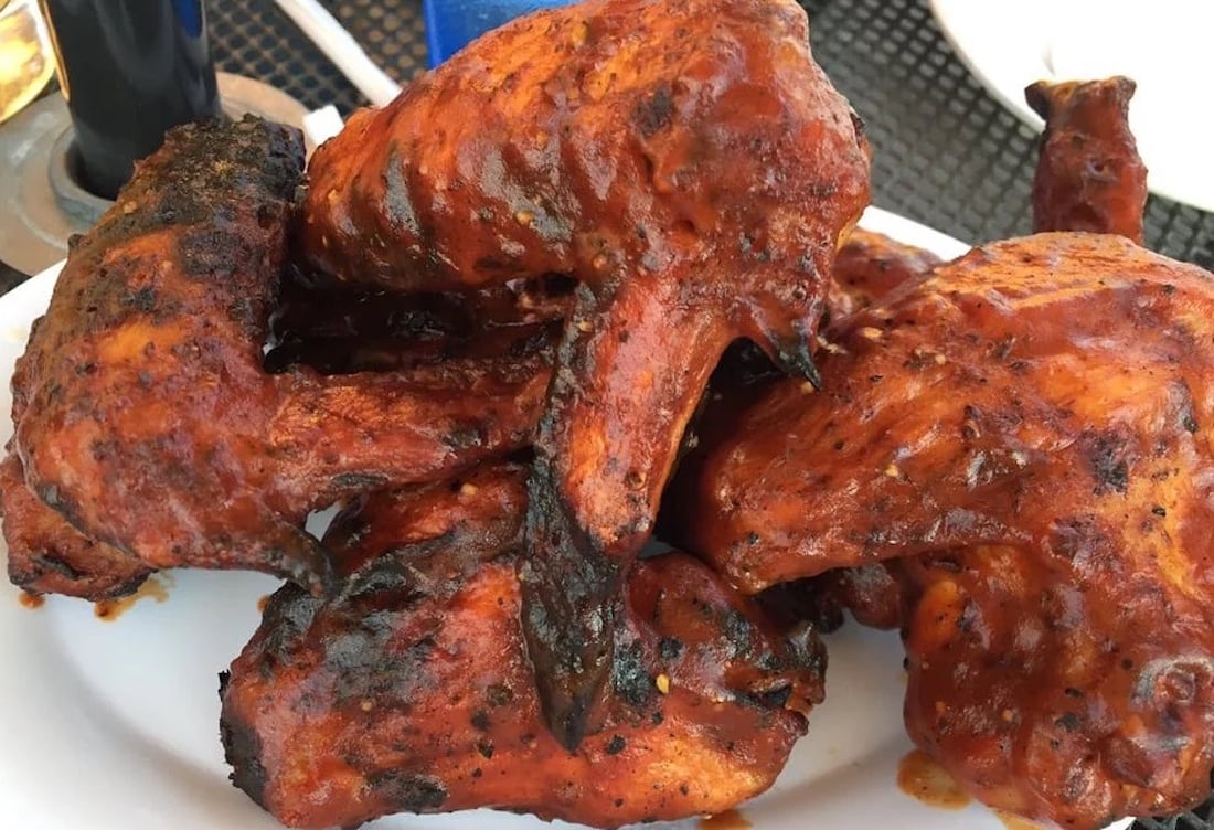 A close-up of several pieces of grilled, saucy barbecue chicken piled on a white plate, with some charred and crispy edges—just like the best chicken wings fresh off the grill.