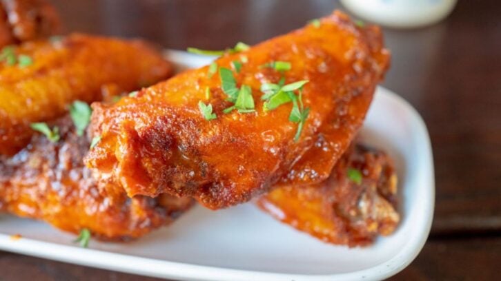 Close-up of the best chicken wings—saucy and crispy, garnished with chopped fresh herbs on a white plate. The glossy, reddish coating hints at a spicy or tangy sauce for bold flavor in every bite.