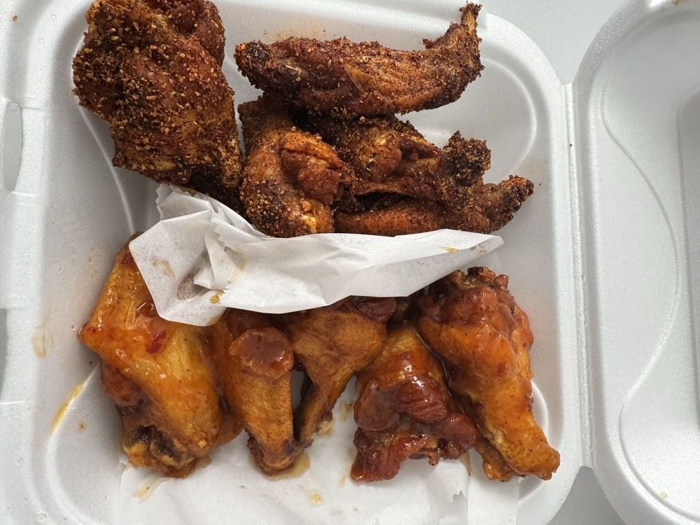 A foam takeout container holds the best chicken wings—crispy fried wings coated in dry seasoning on top, and glazed, saucy wings on the bottom, separated by a piece of white paper.