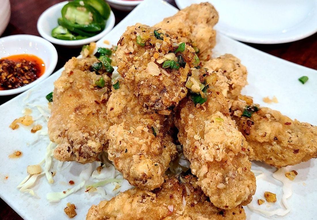 A plate of the best chicken wings, crispy and flavorful, garnished with chopped green onions and garlic, served on shredded cabbage, with sliced jalapeños and chili sauce in small bowls on the side.