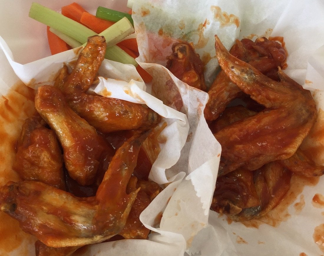 Two baskets lined with white parchment paper, each filled with the best chicken wings tossed in saucy buffalo goodness. In the background, carrot and celery sticks are visible as sides.