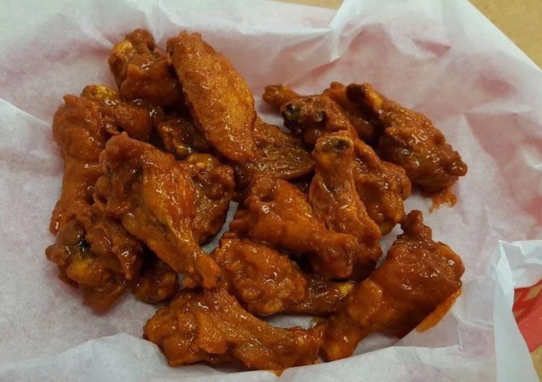 A basket lined with white paper filled with saucy buffalo chicken wings, ready to prove they're the best chicken wings around.