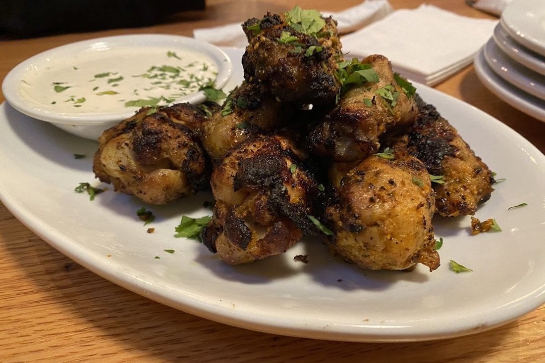 A plate of the best chicken wings, grilled to perfection and garnished with chopped herbs, served with a bowl of creamy dipping sauce on the side, set on a wooden table with stacked plates and napkins in the background.