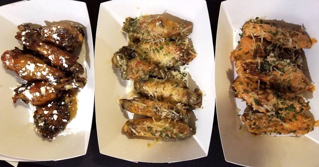 Three trays of the best chicken wings: the left tray features glazed wings dusted with powdered sugar, the middle boasts wings coated in grated cheese and herbs, and the right has saucy wings topped with shredded cheese and herbs.