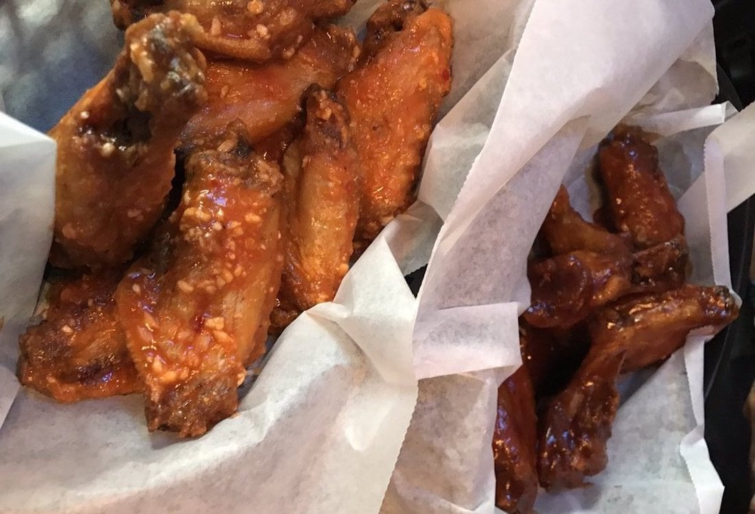 Two paper trays filled with the best chicken wings—one coated in a light garlic sauce, the other in a rich barbecue or spicy glaze—sit atop crisp white parchment paper, tempting your taste buds with every bite.