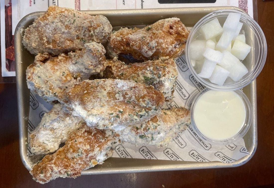 A tray of the best chicken wings, perfectly seasoned and fried, topped with herbs, served alongside a cup of white dipping sauce and cubed pickled radish.