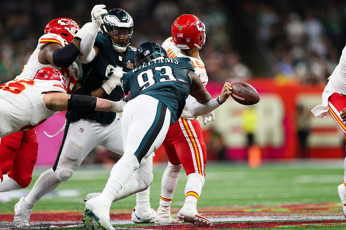 A football player in a dark green Philadelphia Eagles uniform attempts to sack the Kansas City Chiefs quarterback, who is holding the ball, during an intense NFL game where Super Bowl ticket prices are at an all-time high. Other players surround them in action.