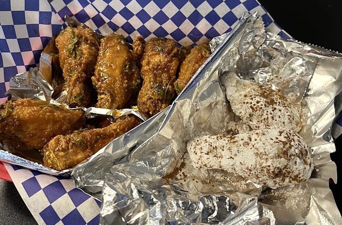 A tray with the best chicken wings: one side coated in a dark, sticky sauce, the other dusted with white powdered sugar—all served on foil and blue-and-white checkered paper.