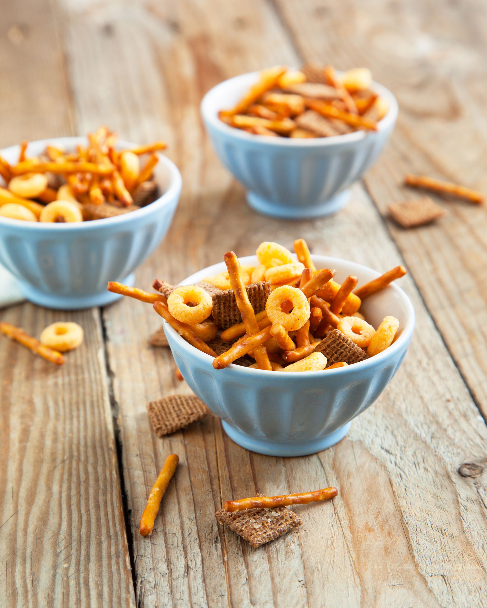 Three blue porcelain bowls of original chex party mix on a wooden table
