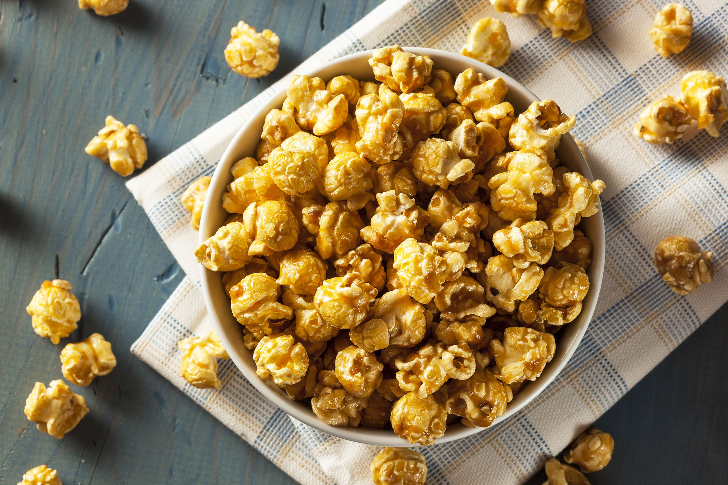 Top view of seasoned popcorn in a white bowl on a blue and orange checkered napkin on a blue table