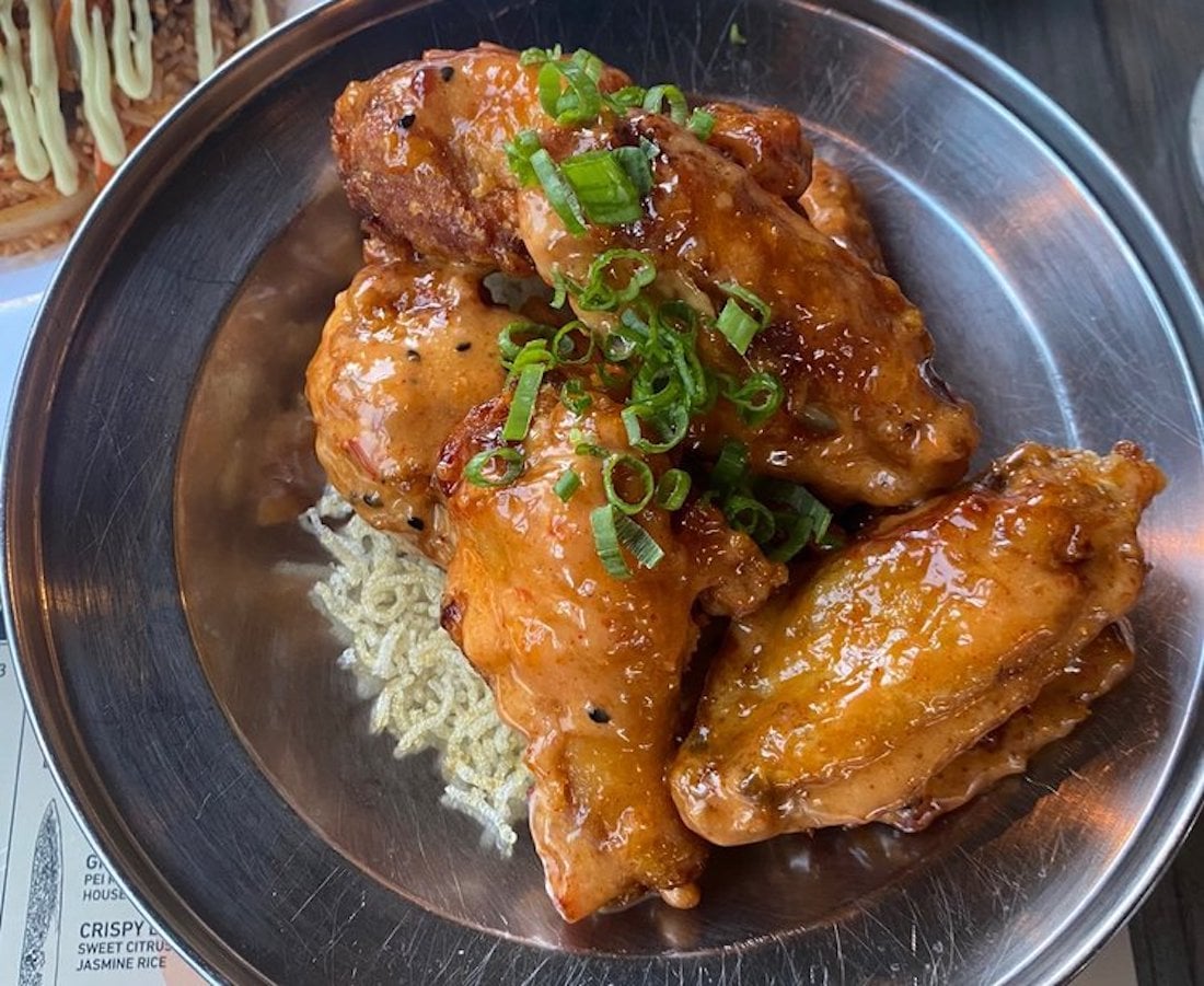A metal plate filled with the best chicken wings, glazed to perfection and garnished with chopped green onions, served on a bed of crispy noodles.