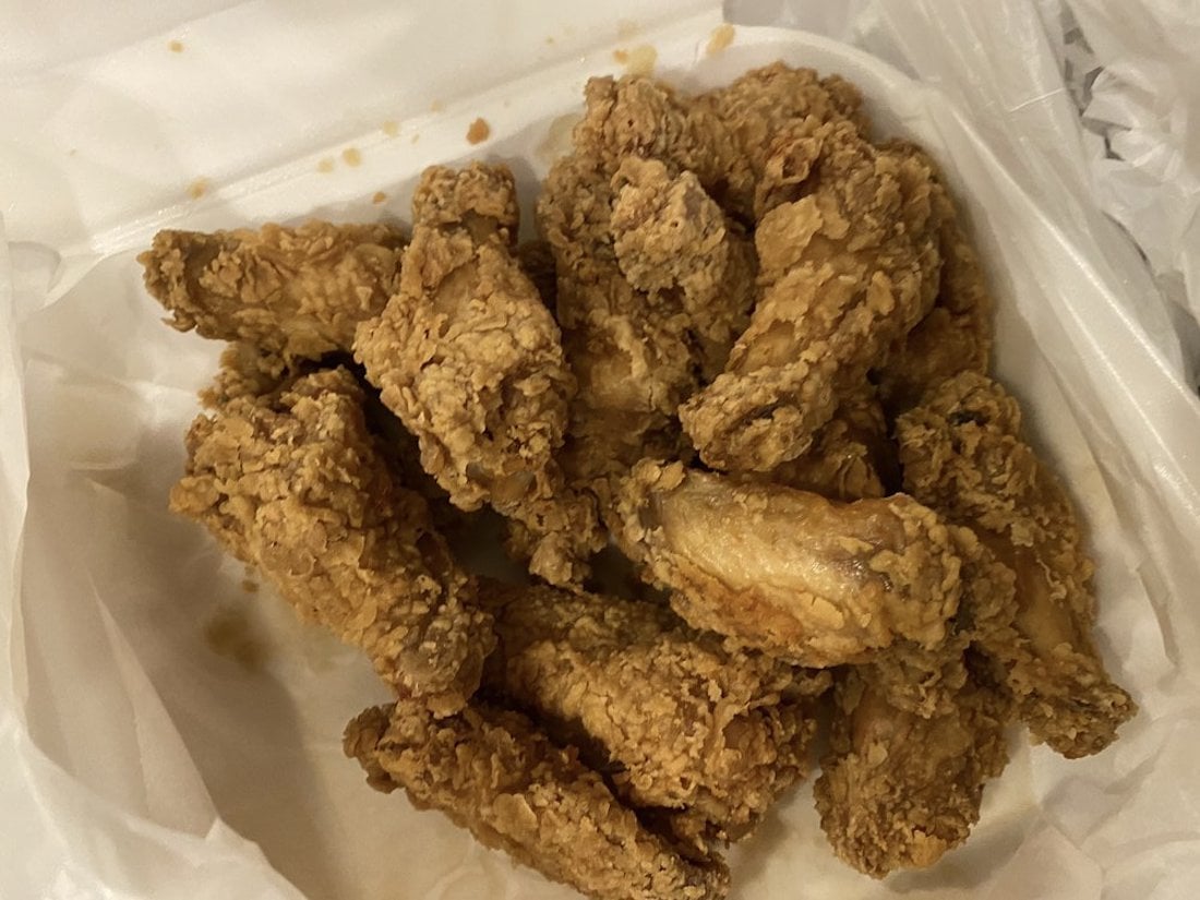 A pile of golden-brown fried chicken wings—some of the best chicken wings you’ll find—rests on white wax paper inside a food container.