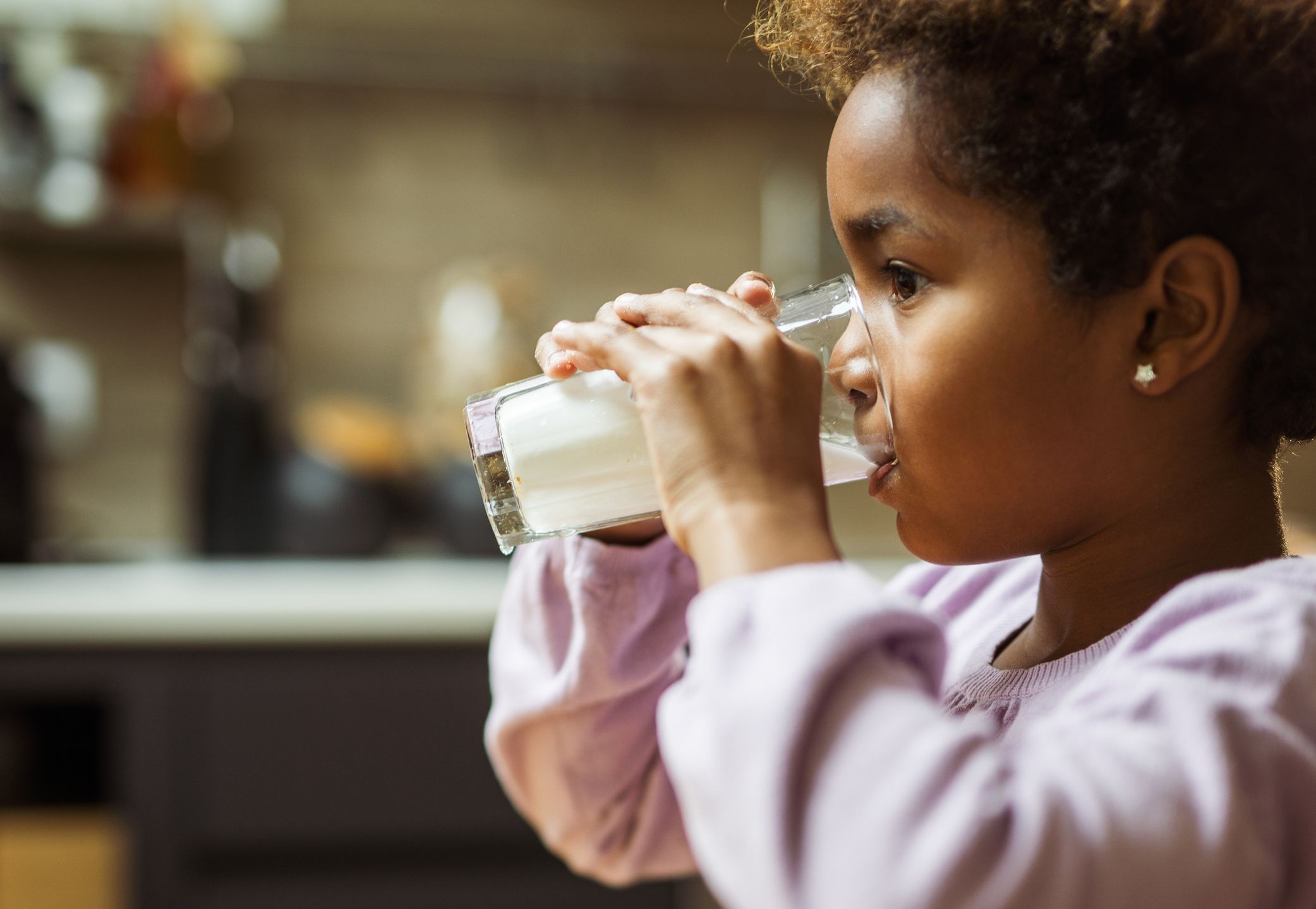 Little African American girl drinking fresh milk from glass at home.