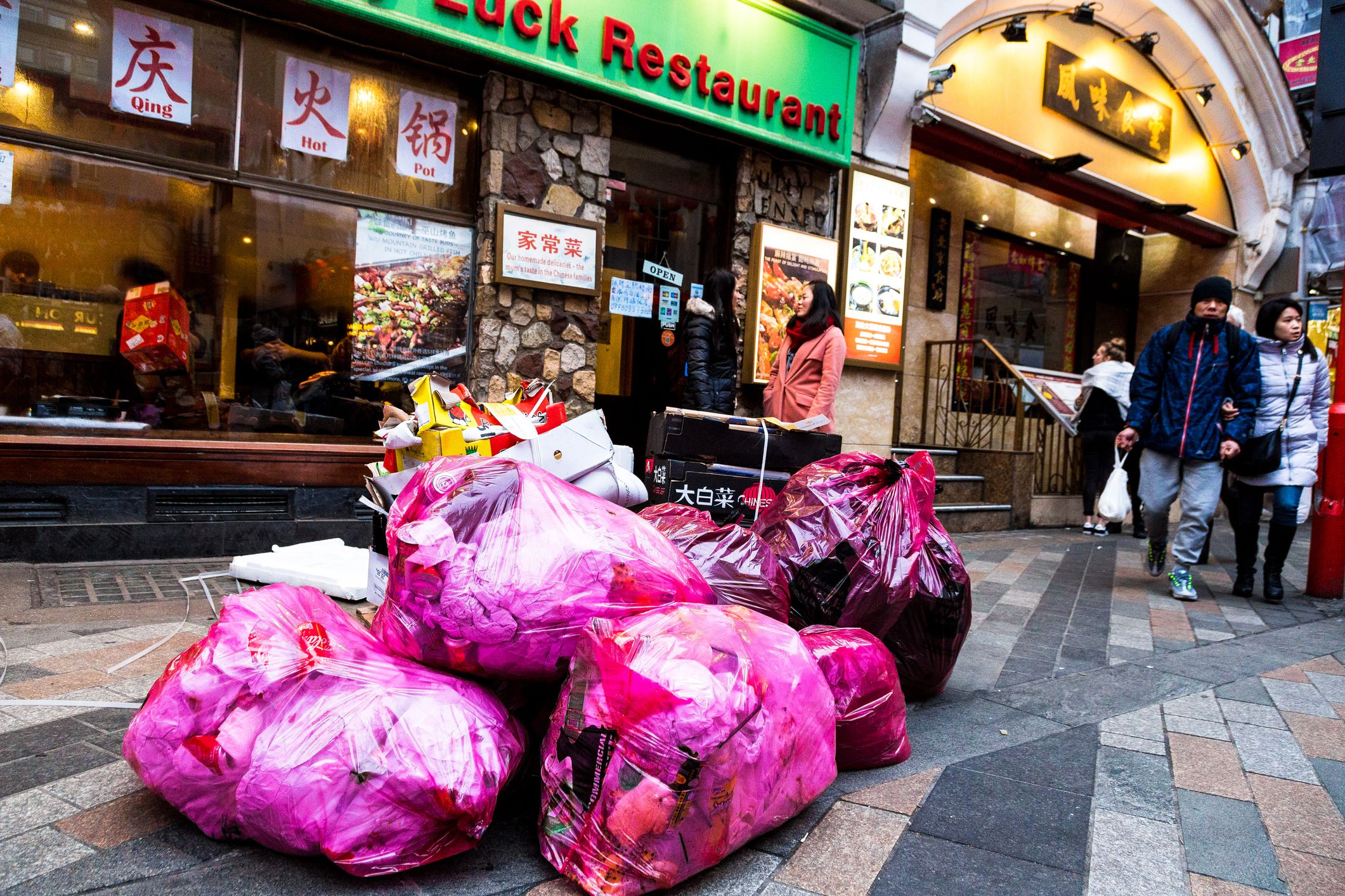London, UK - 5 February, 2019: color image depicting multiple trash bags full of waste food on a city street outside a Chinese restaurant in Chinatown, London, UK. People can be seen on the street in the background. Room for copy space.