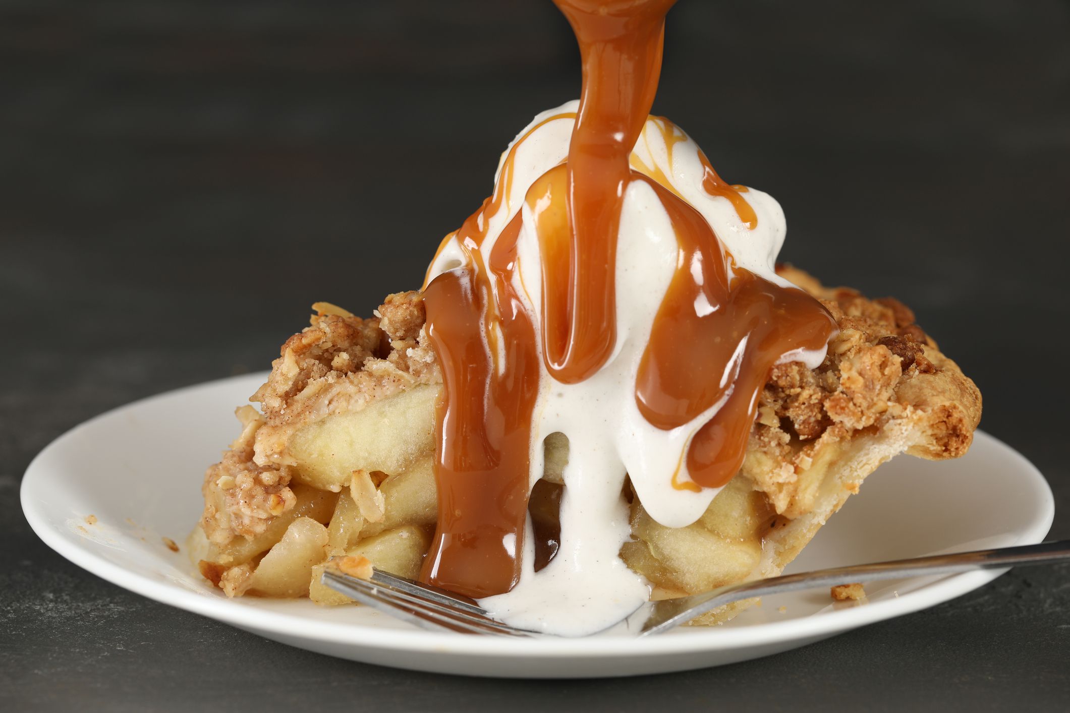 Extreme close up horizontal photograph of a slice of apple pie å la mode being treated to a caramel pour.Isolated on black