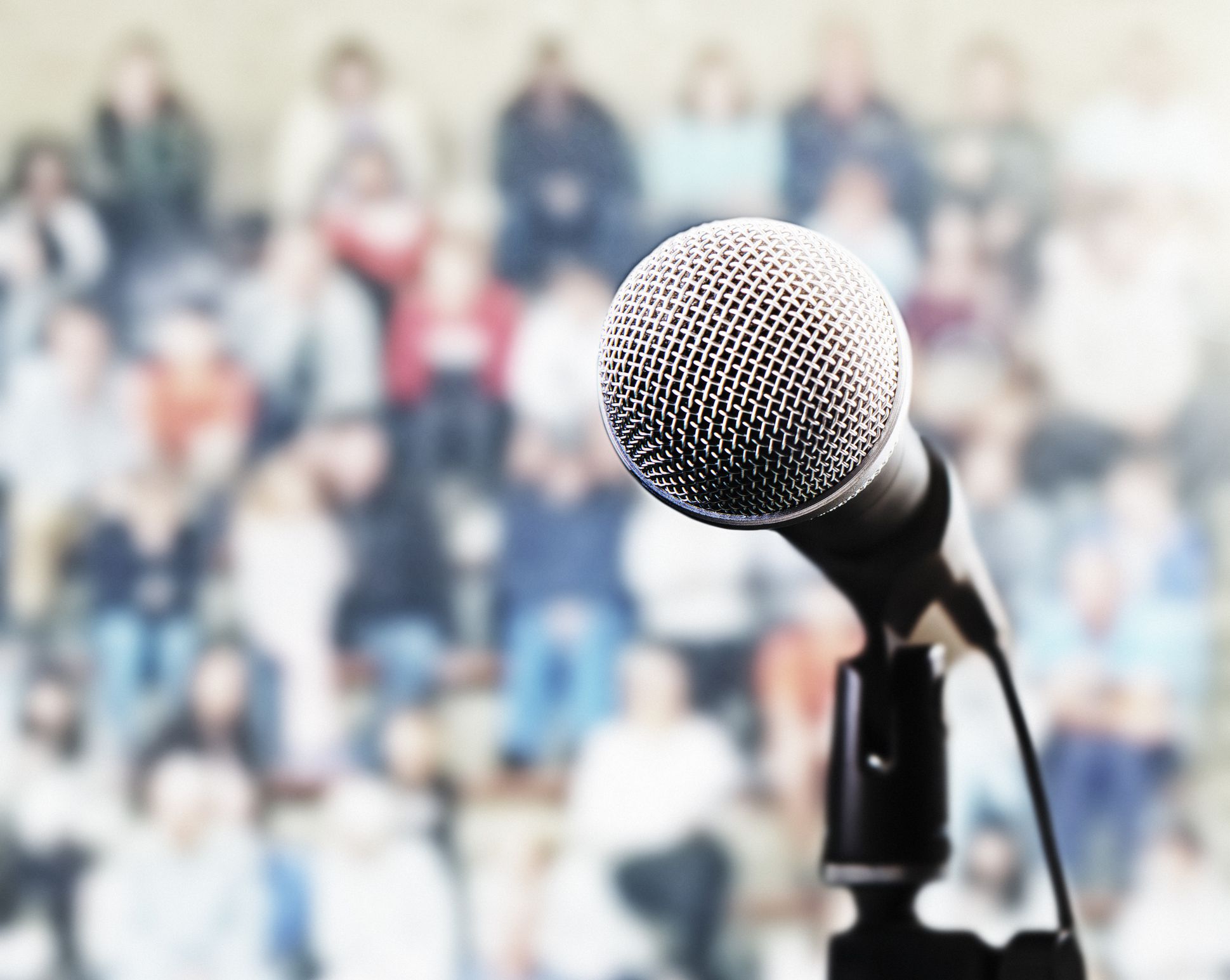 A microphone on a stand in front of a large, defocused audience.
