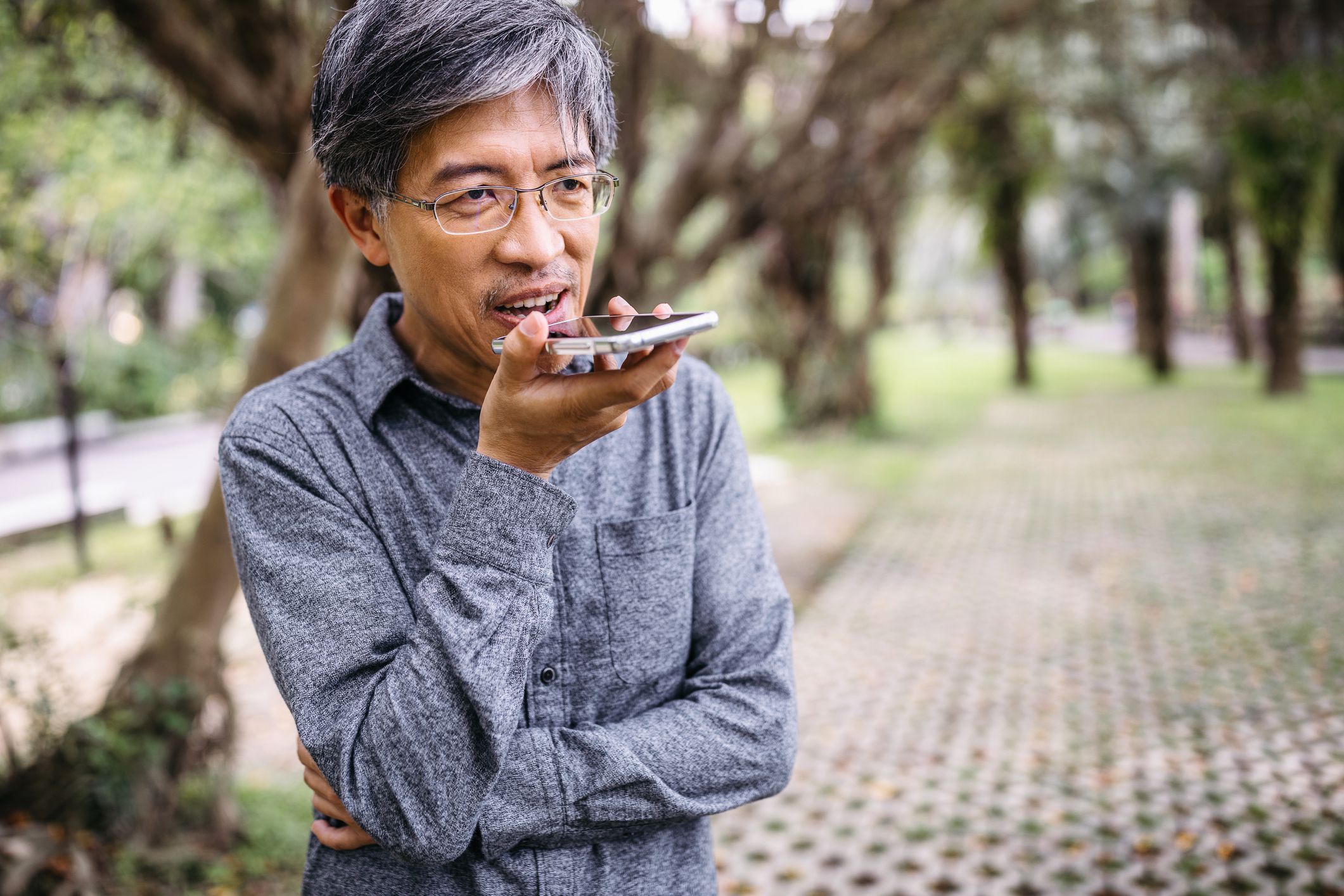 Senior Asian man using smartphone, recording audio message in the park