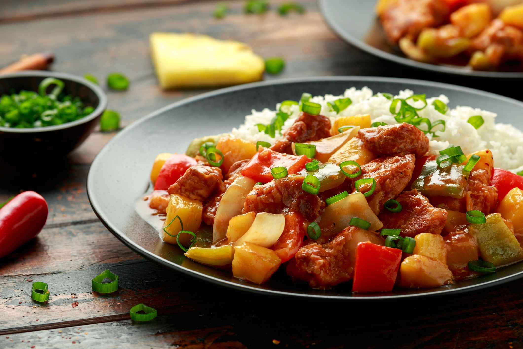 Pineapple and Chicken in sweet and sour sauce with bell pepper, rice and spring onion in black plate.