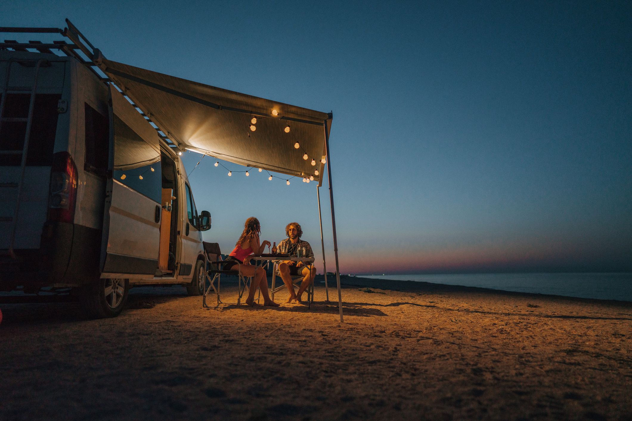 Young Caucasian heterosexual couple near the camper van parked near the sea at sunset