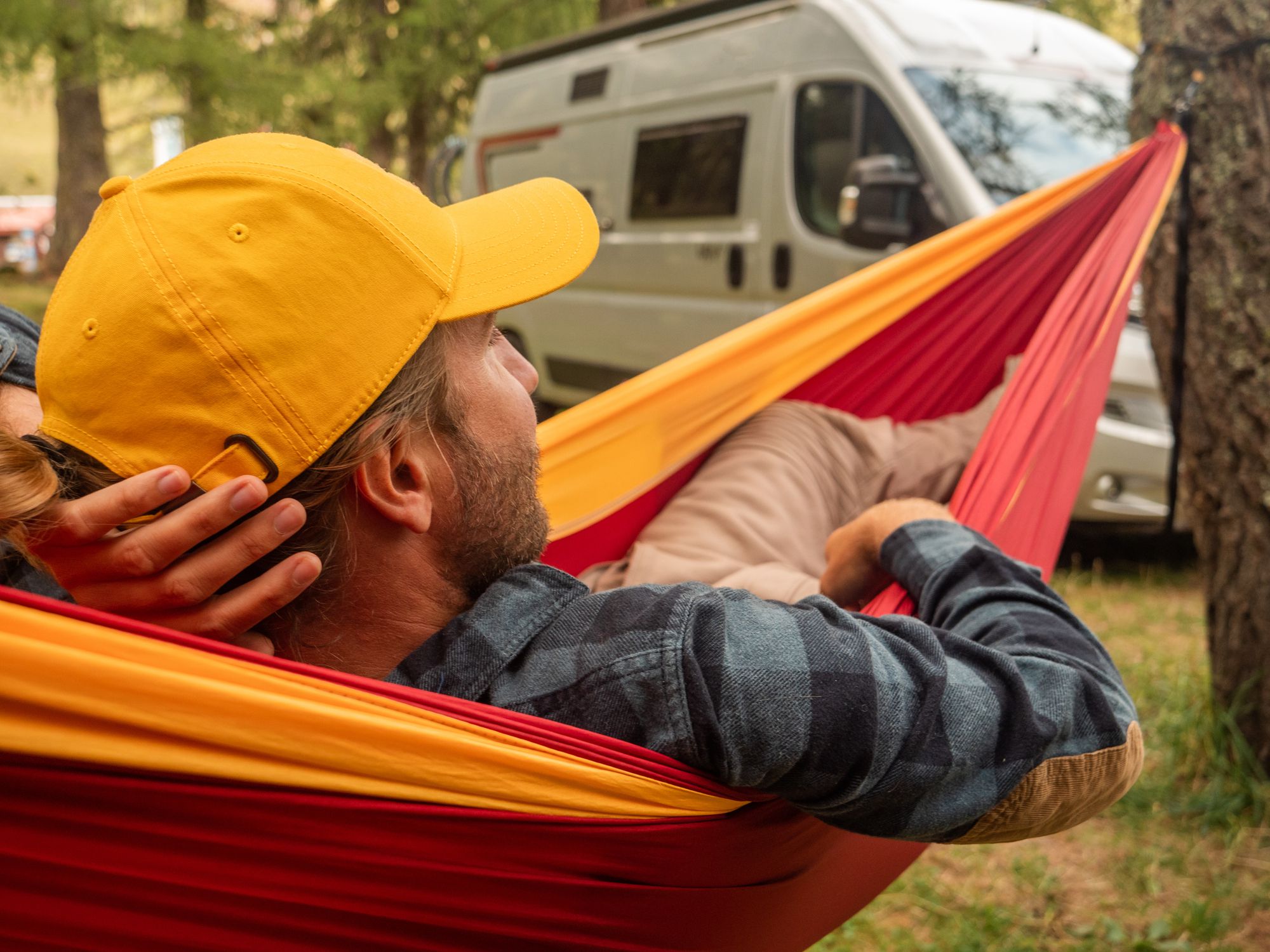 He lies on red hammock at sunset, forest in distance