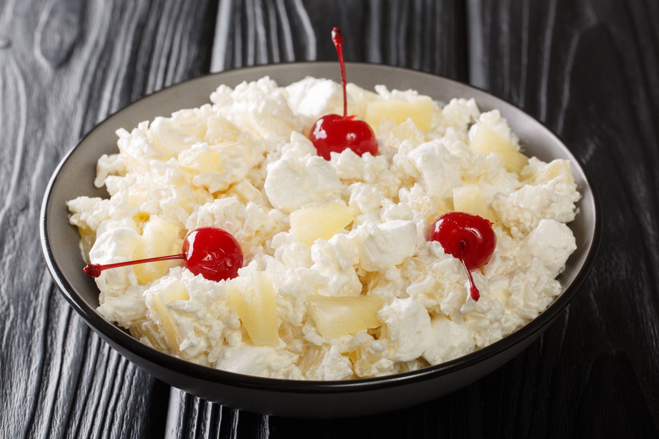 Glorified Rice is a cold dessert salad made with rice, crushed pineapple, maraschino cherries, and marshmallows tossed with a whipped cream close-up in a plate on the table. Horizontal