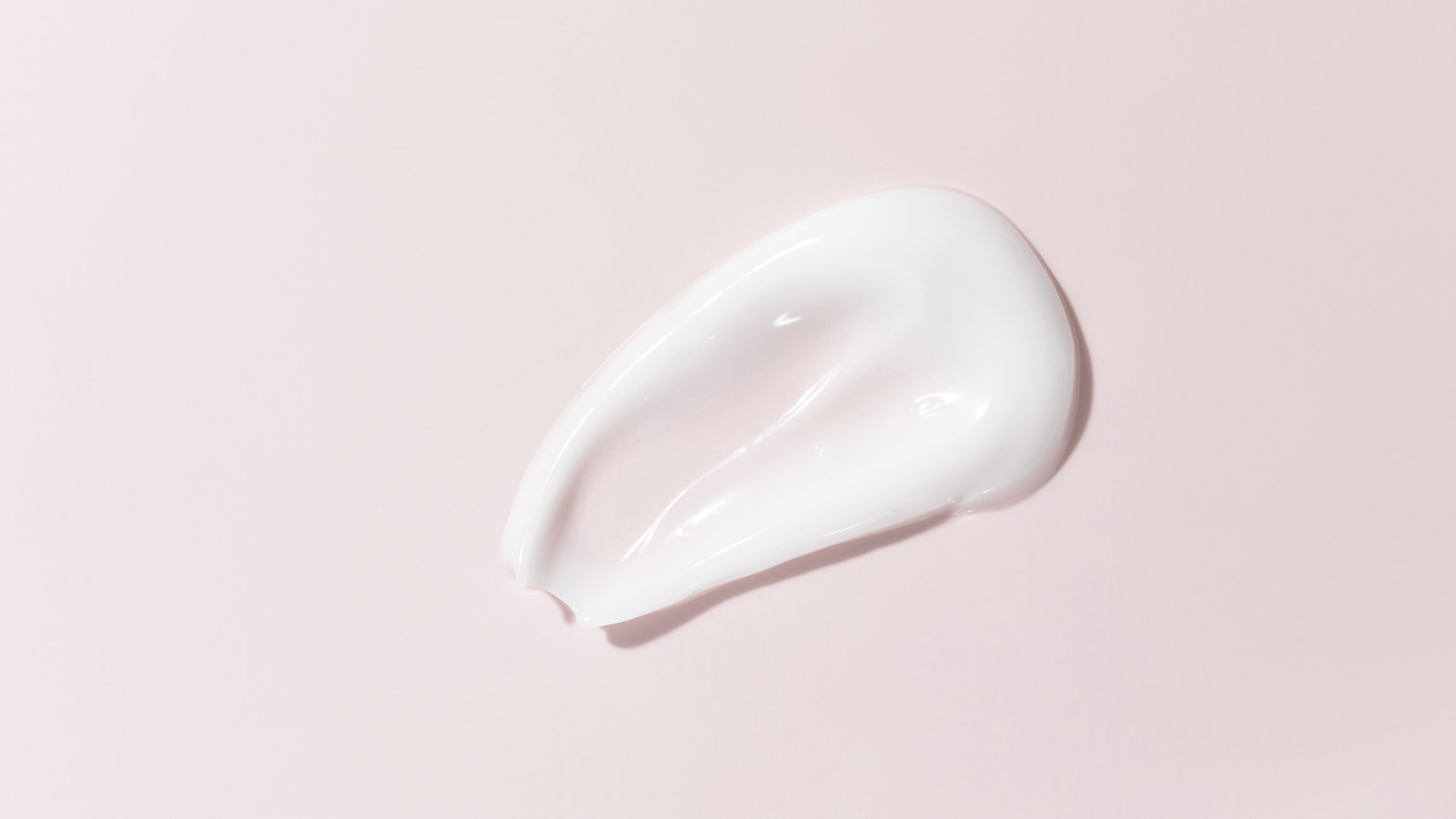 White beauty cream smear smudge on pink background. Cosmetic skincare product texture. Face cream, body lotion swipe swatch. High quality photo