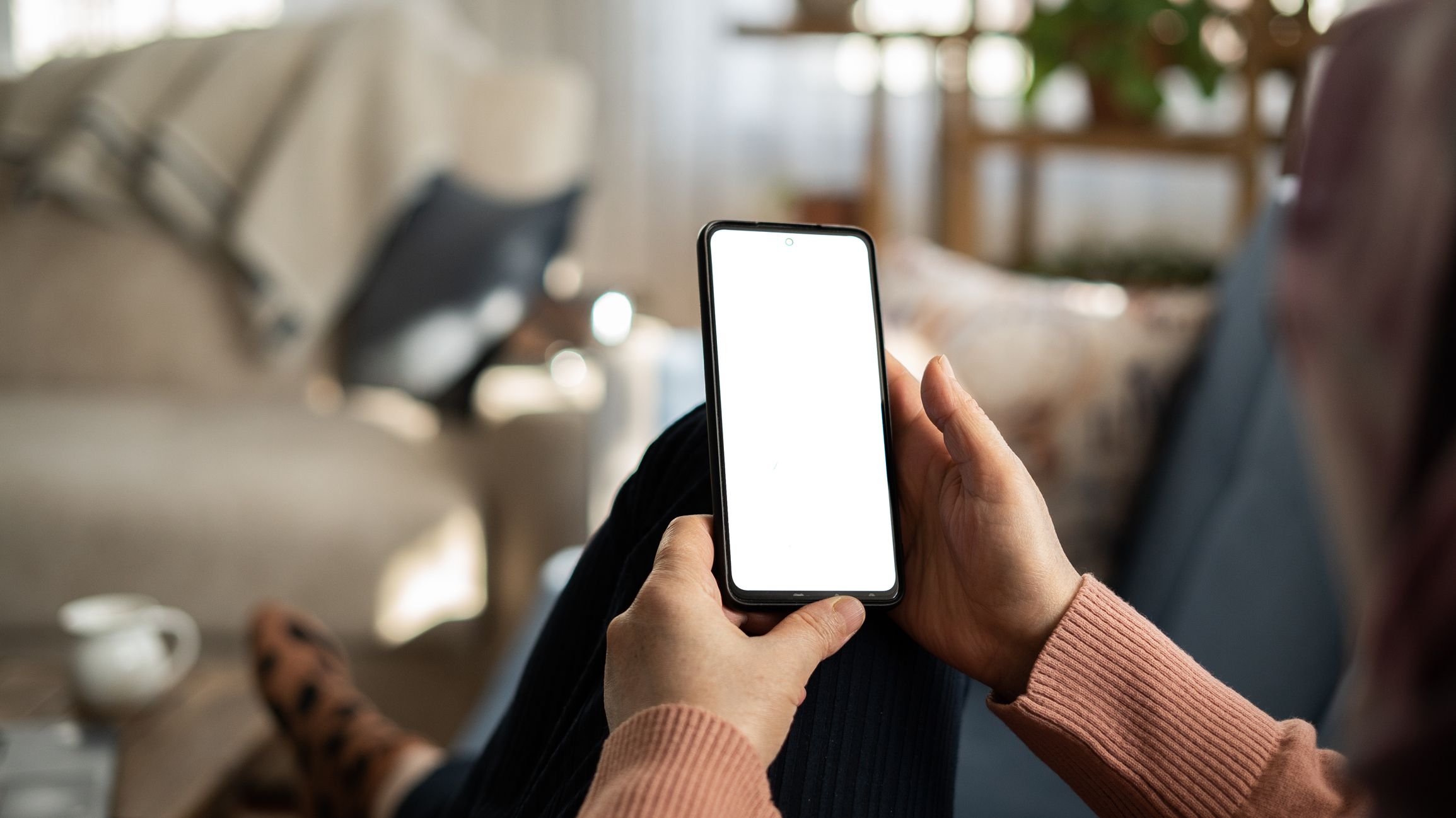 Woman using phone with white screen while lying on sofa at home , mock up screen