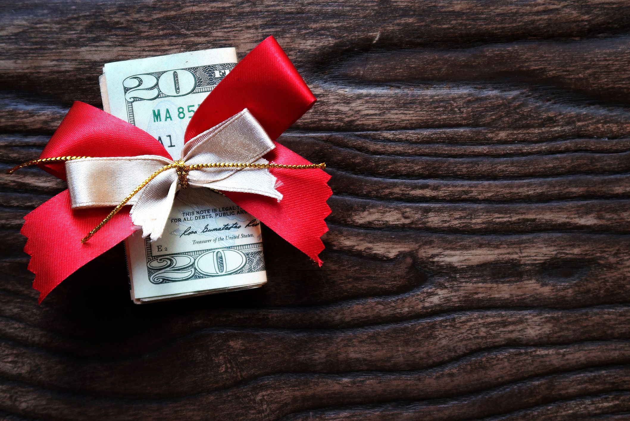 Money gift on wood copy space background, cash dollar banknote with beautiful red gold ribbon, concept of cash give on holiday, year end bonus for employee, Christmas holiday shopping budget