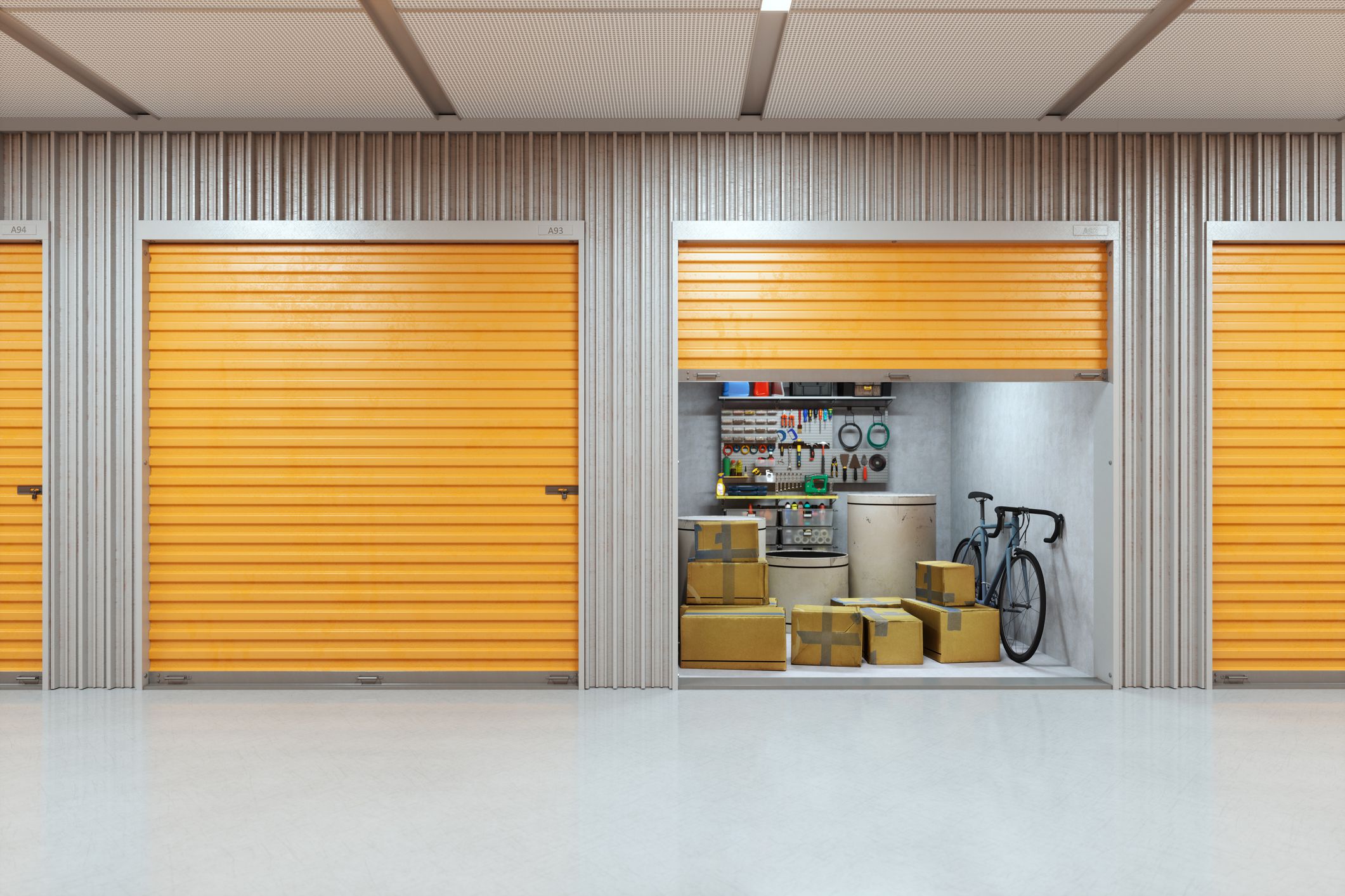 An organized self-storage facility featuring orange storage doors.Inside the unit a bicycle leaning against the wall, cardboard boxes, and an array of tools displayed.