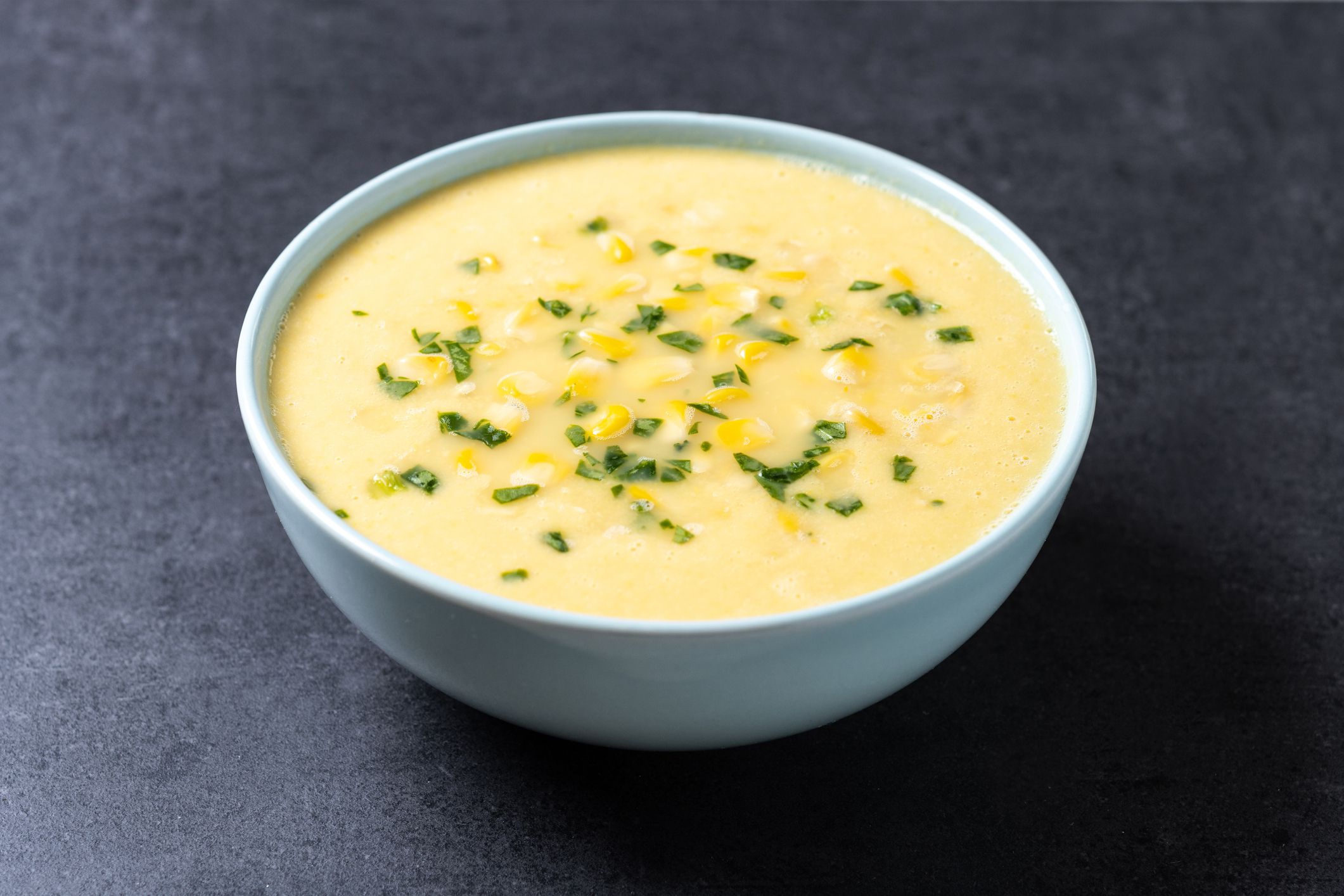 Corn soup in white bowl on black background