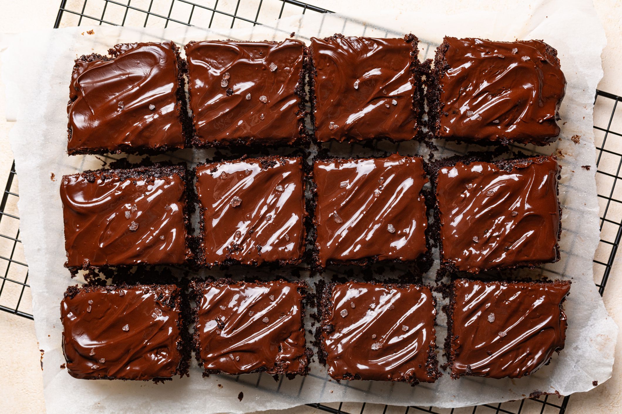 Cut peaces of dark chocolate moist buttermilk sheet cake with chocolate butter cream, homemade dessert on a cookig resting tray and baking paper.