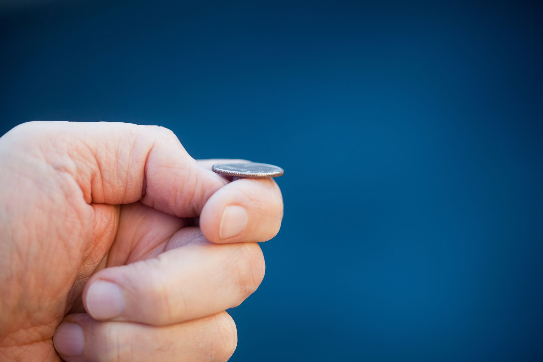 Hand ready to flip coin. Blue background.