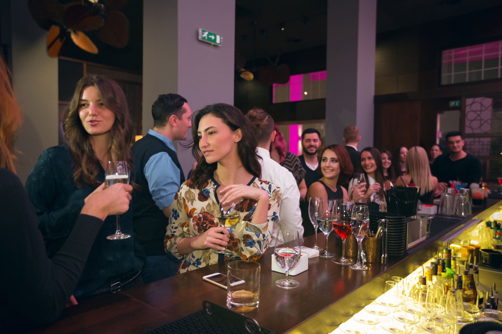 Group of people standing by bar counter, dinking cocktails