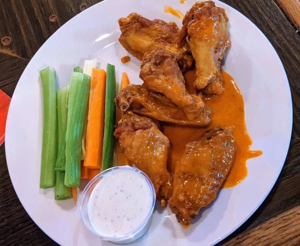 A plate of the best chicken wings covered in buffalo sauce, served with celery and carrot sticks, and a cup of ranch dressing on the side.
