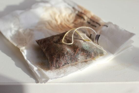 A used tea bag rests on several folded, stained paper napkins atop a white surface, with sunlight casting soft shadows.