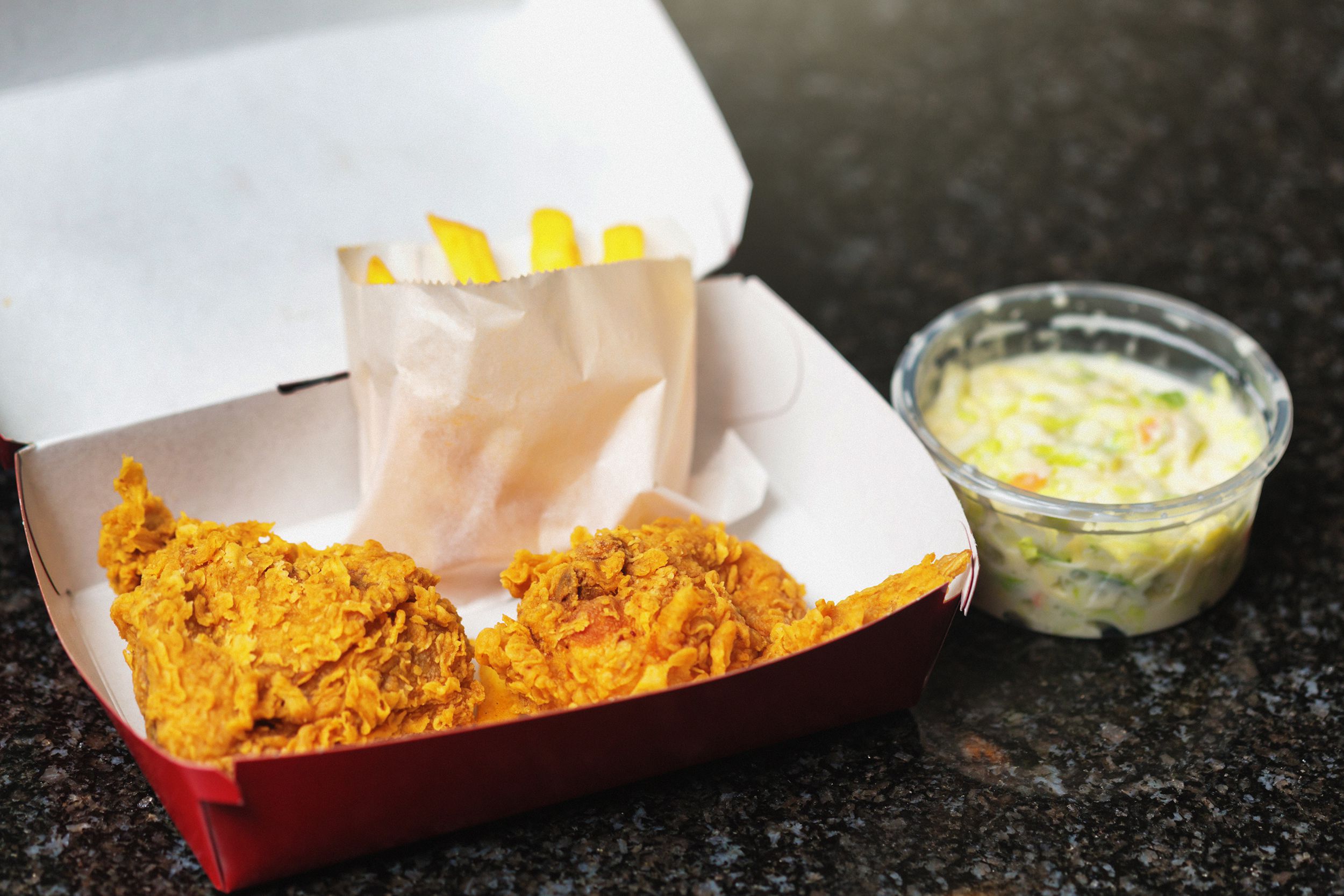 carton of fast food fried chicken with fries and a side of coleslaw