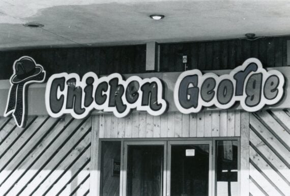 Black and white storefront sign for Chicken George with a stylized hat logo above the name.