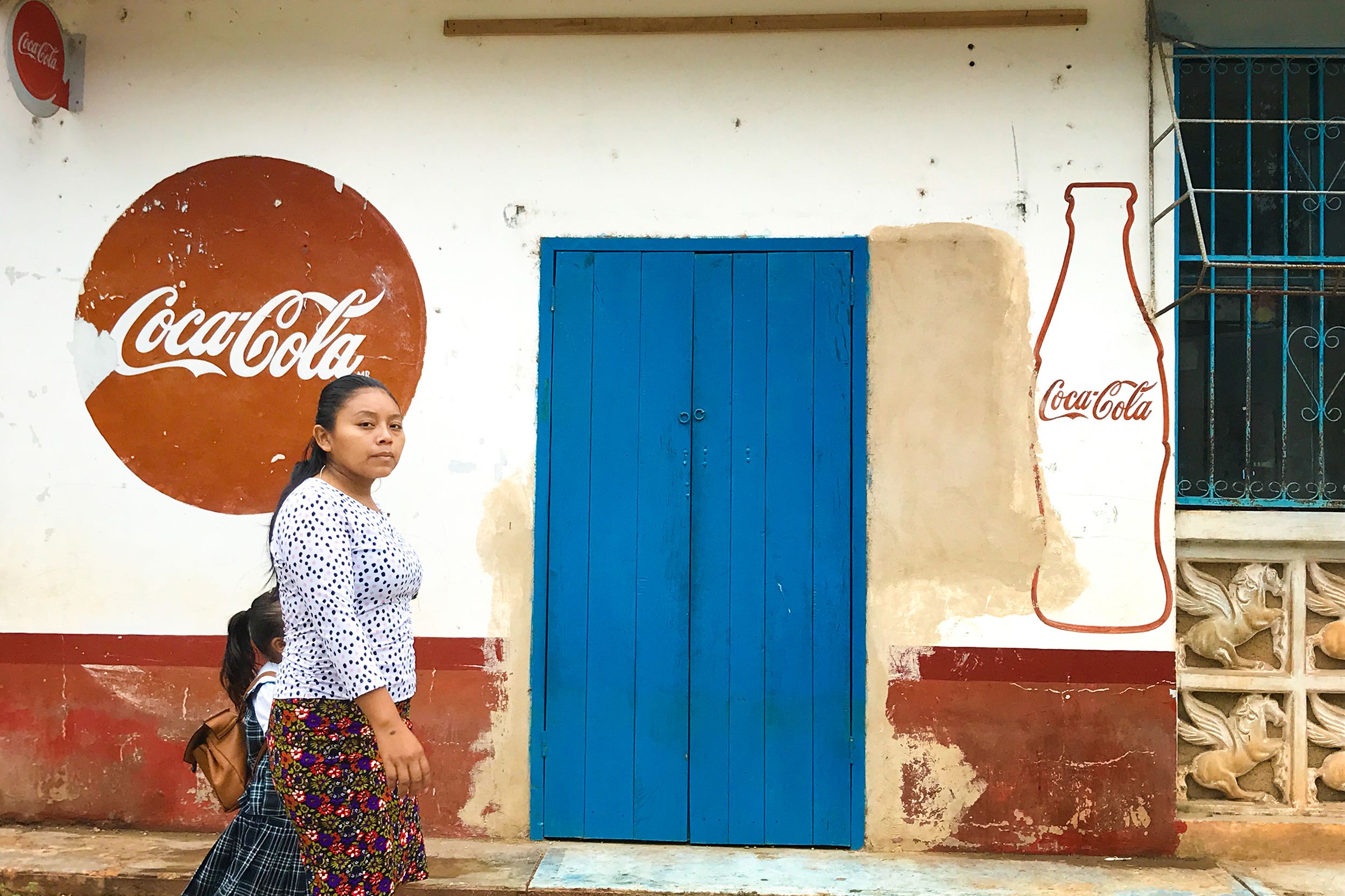 young woman walks with her daughter past a mini market in Dzitnup, Mexico