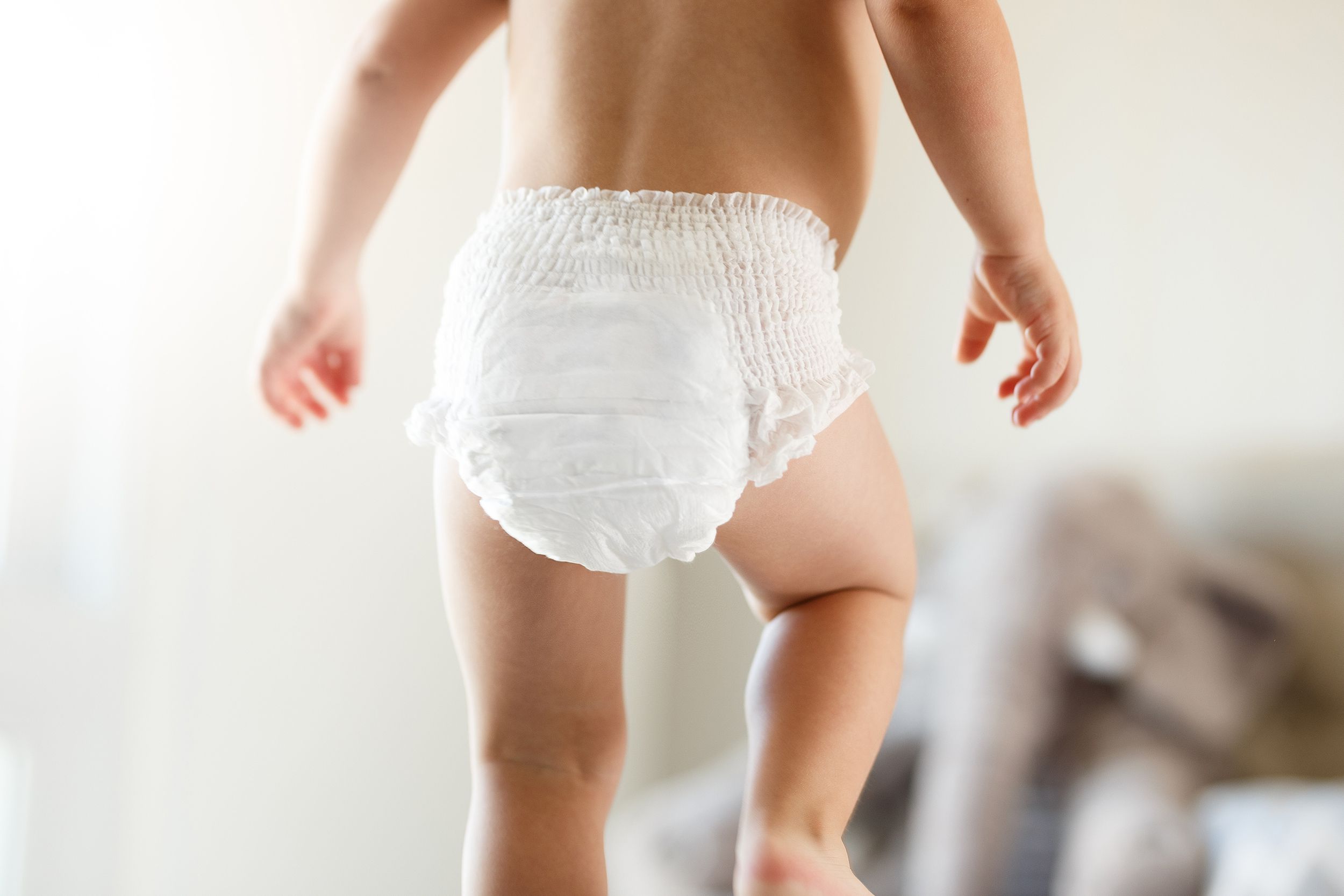 Baby in diaper, showing backside with blurred background of living room