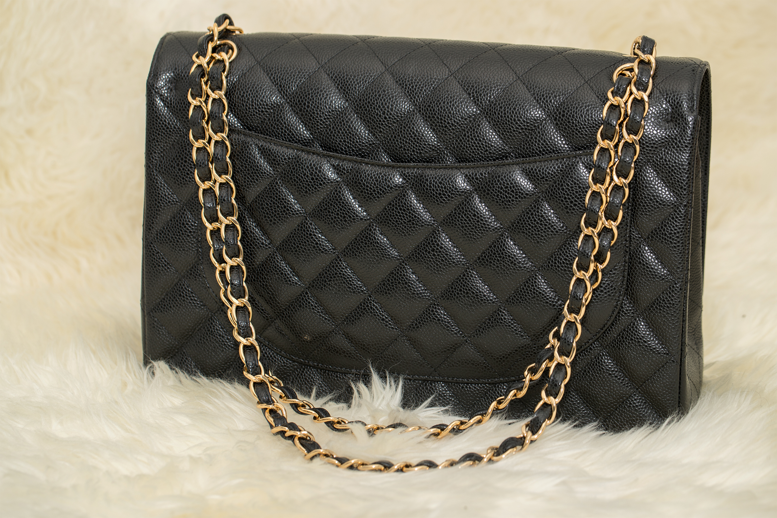 Black leather designer purse with a gold chain on a light pink shaggy rug