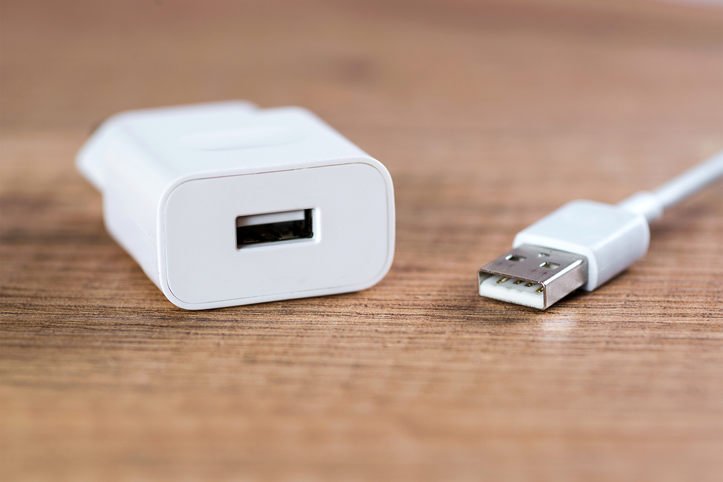 Closeup of white mobile phone charger with USB cable, selective focus, on a wooden veneer table