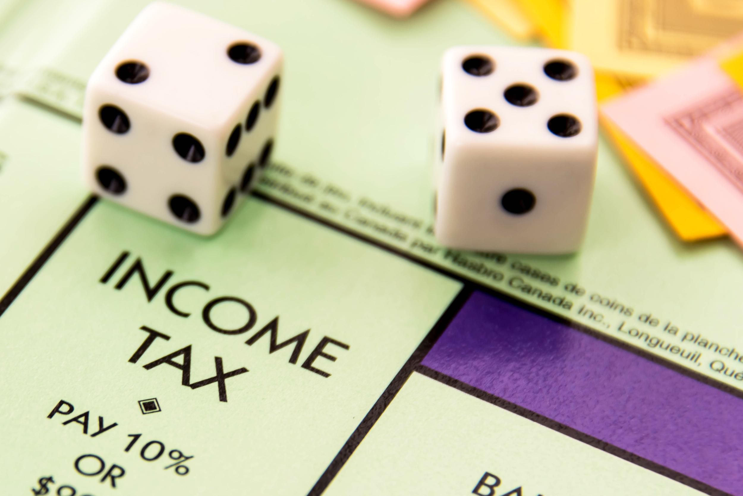 Dice on Monopoly board, focus on income tax square, with Monopoly money in background
