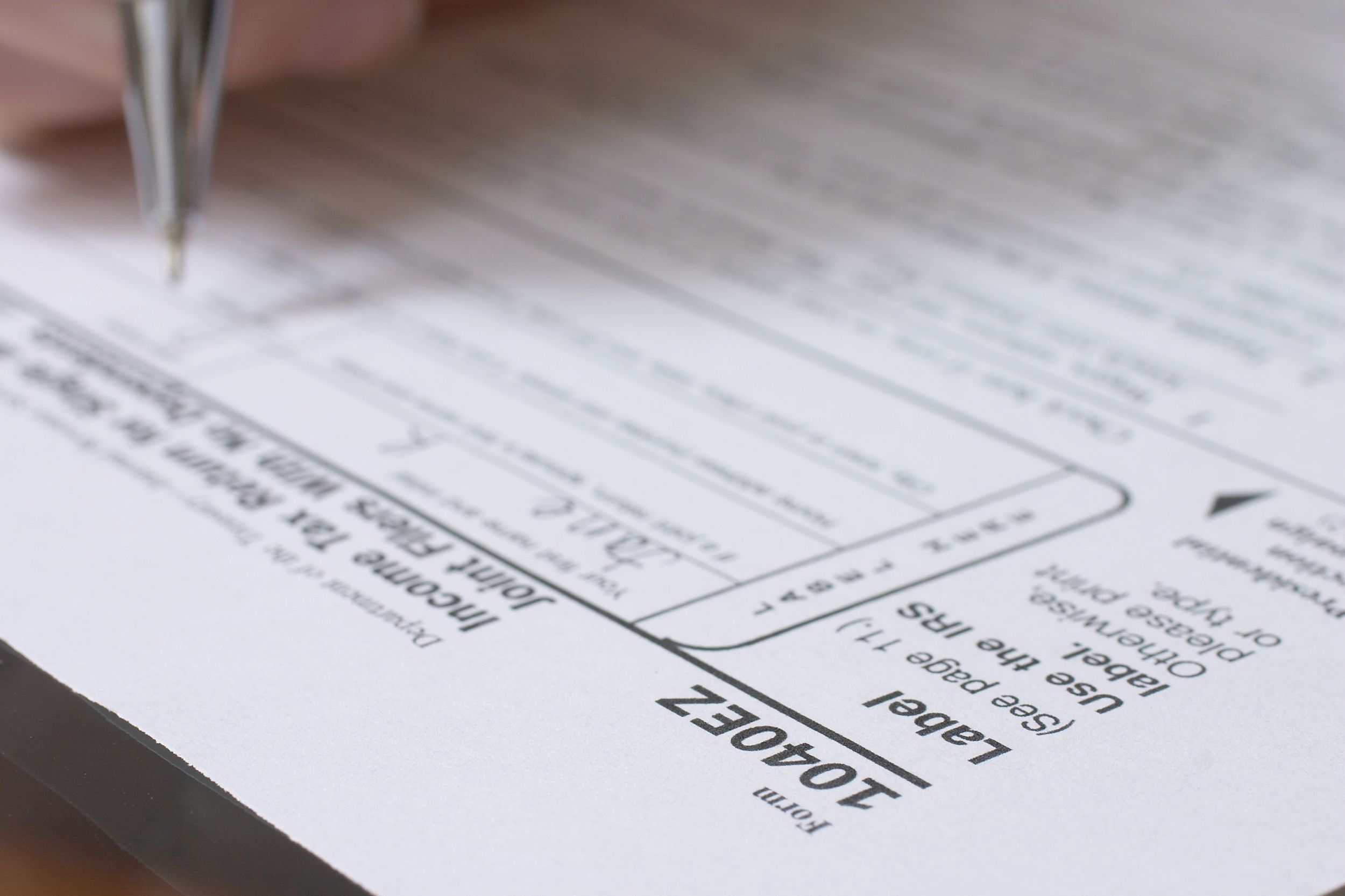 Hand with pen on IRS 1040EZ form on table