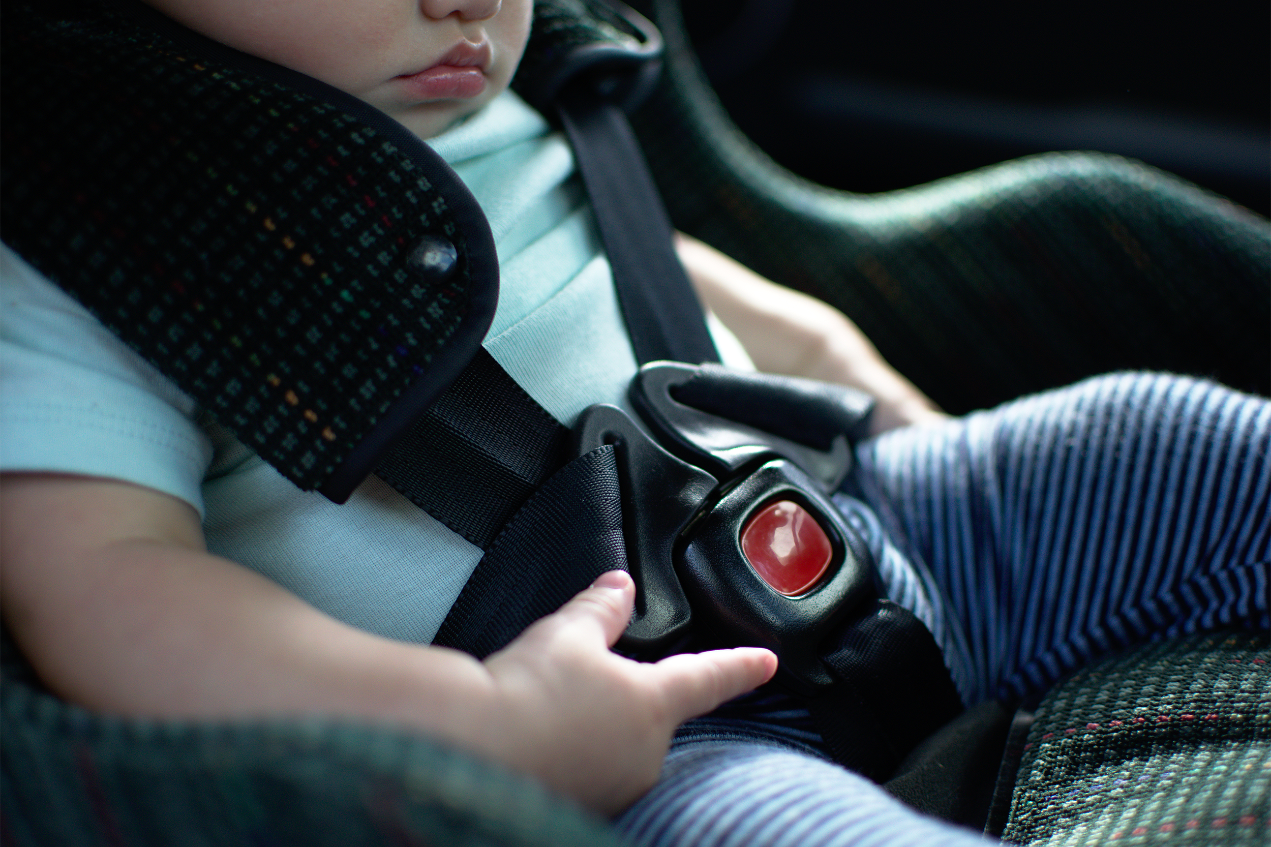 Mid-section of baby in rear facing car seat, focus on secured safety belt buckle, with a blurred background in car