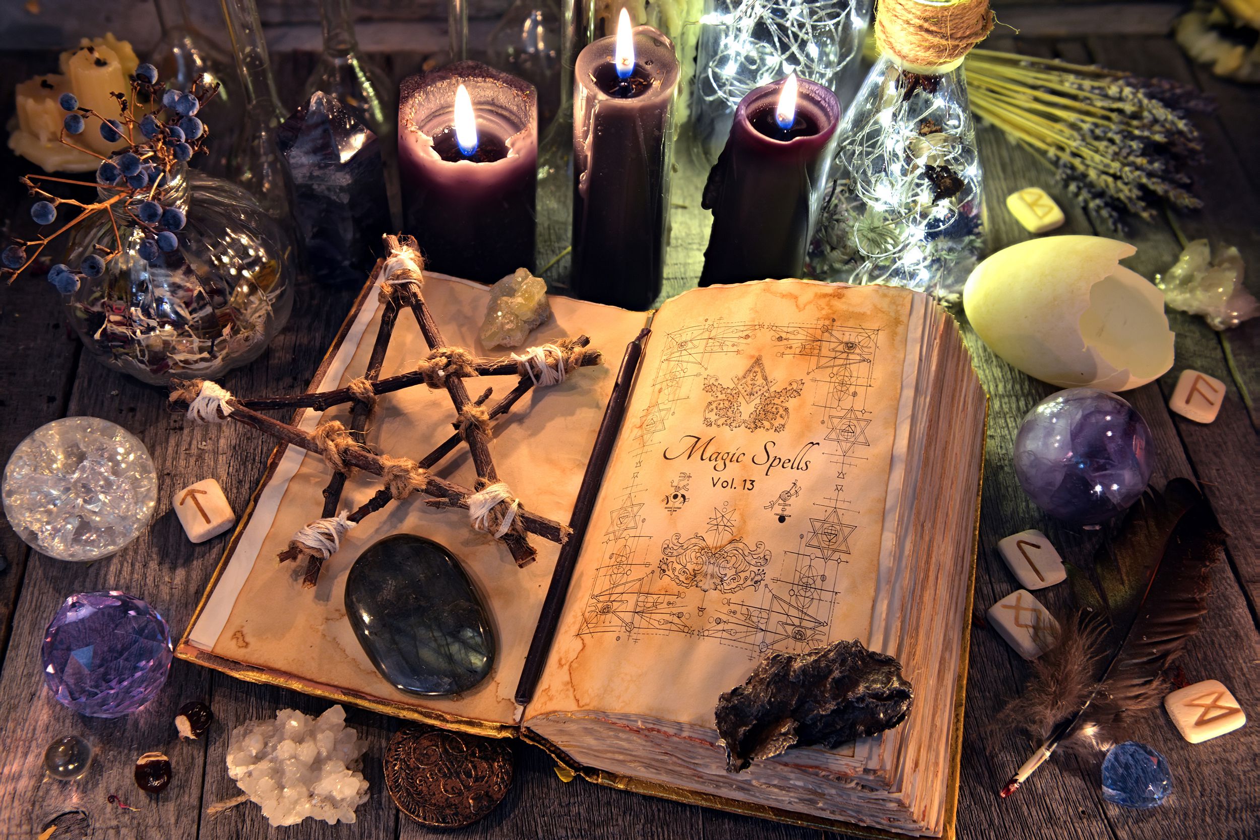 Old witch craft book with pentagram and a few crystals, surrounded by black candles, crystals, and other ritual objects