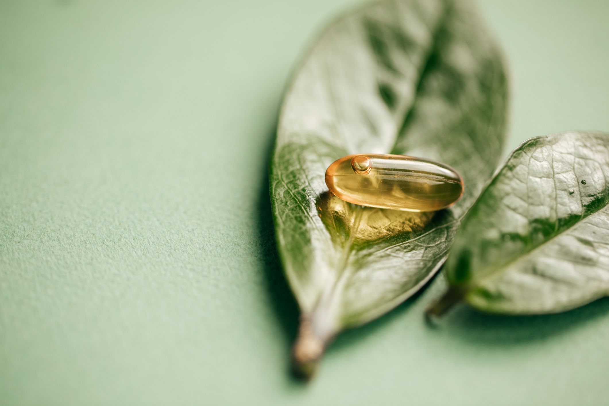 One clear yellow pill on a green leaf, selective focus, with another leaf on the right, sage green table on the left