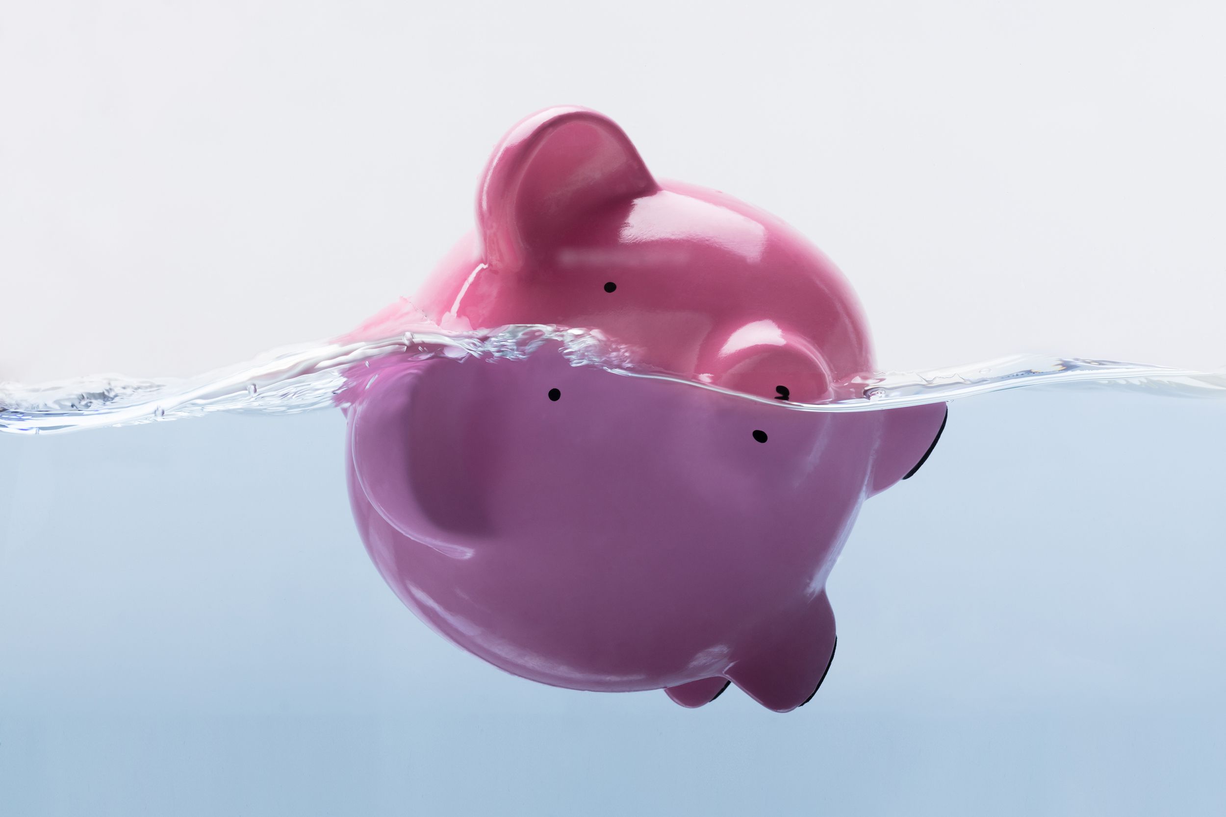 Pink piggy bank floating sideways in water, half submerged