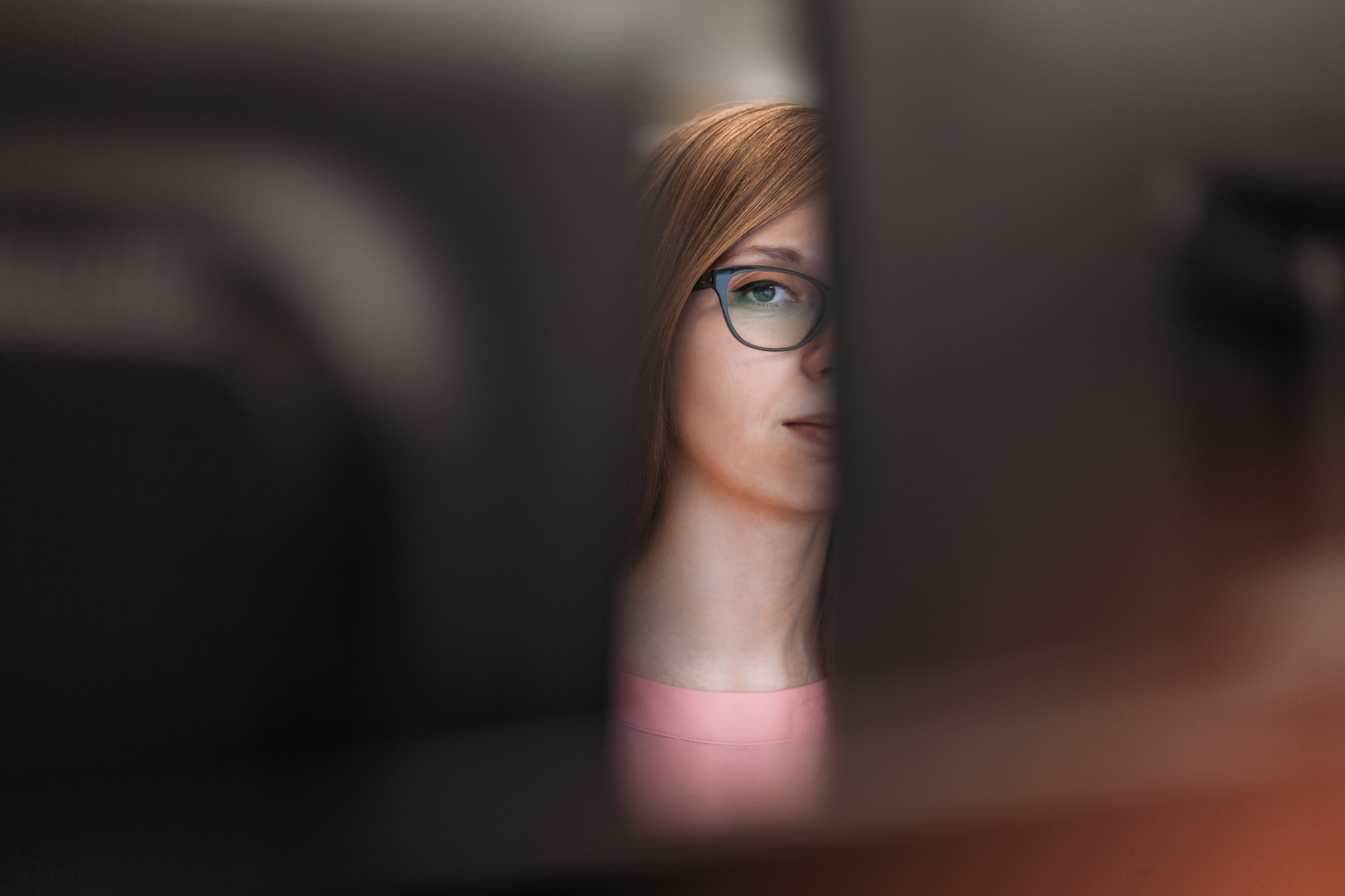 Resentful woman peeking between two black monitors at an office, selective focus, black monitors blurred in the foreground
