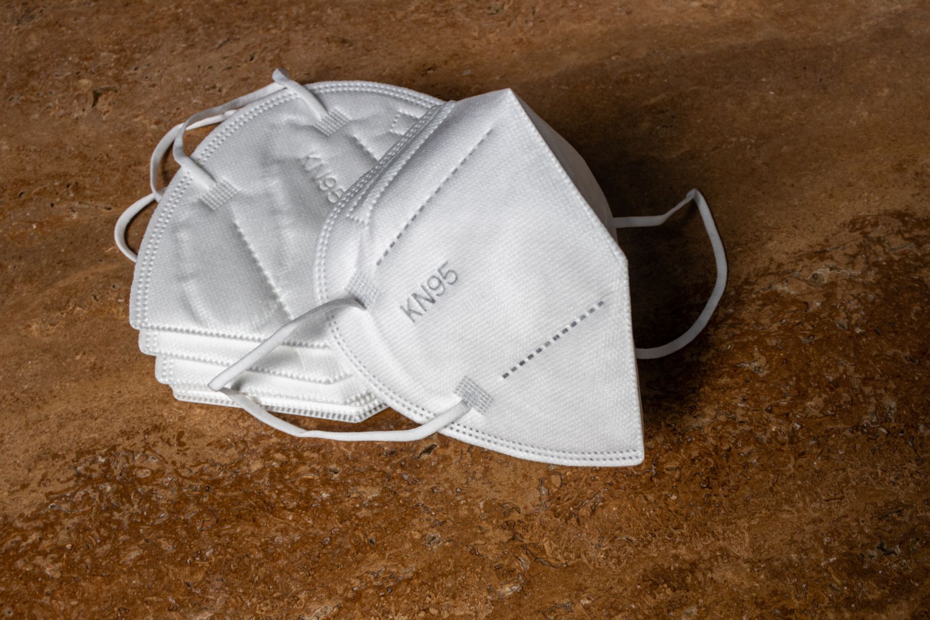 Stack of white KN95 disposable masks, one is leaning on top of them, on a brown background