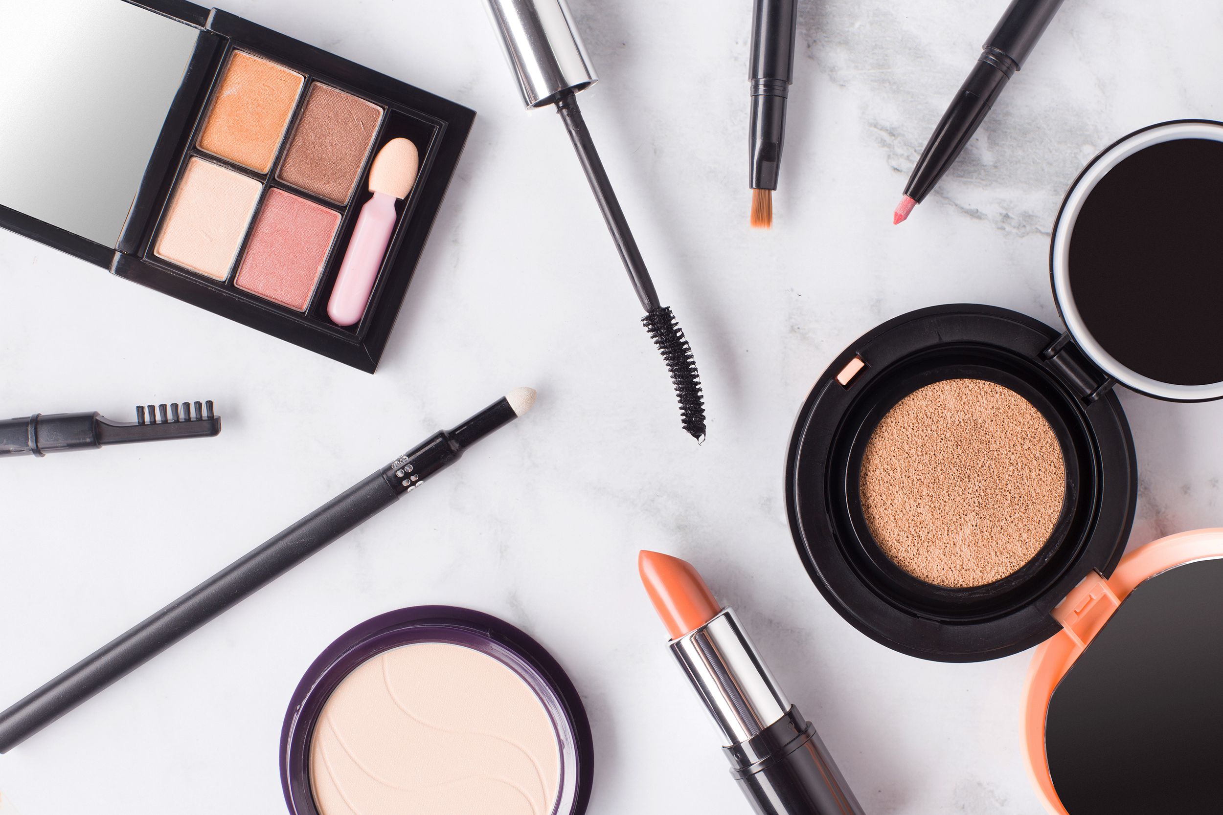 Top-view of many different types of cosmetics on marble, mascara, lip stick, blush, eye shadow, and more